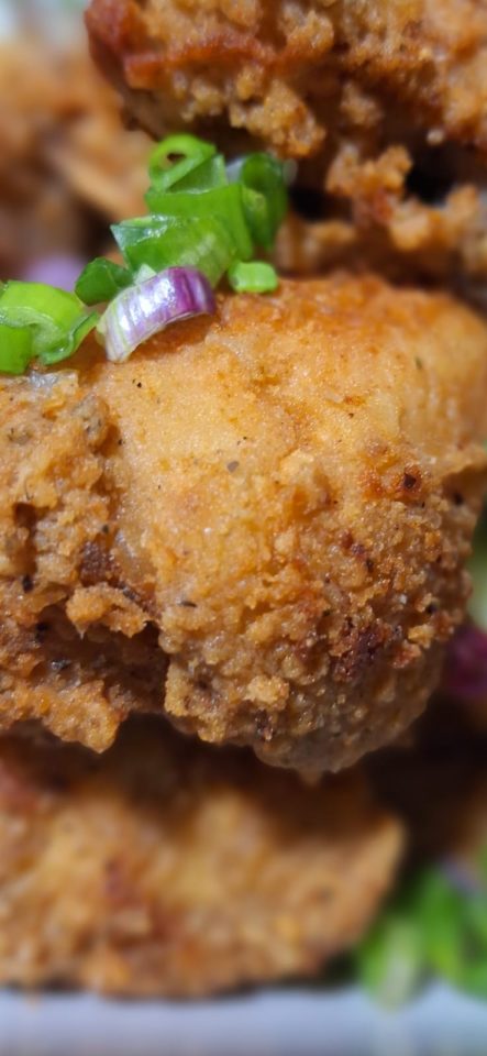 Close-up of crispy fried chicken pieces garnished with green onions and herbs.