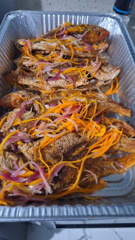 Fried fish garnished with sliced onions and orange carrots in a foil tray.